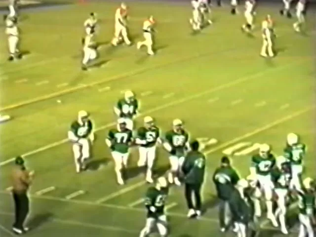 A videotape frame from 1986: players in green jerseys on a lit field, seen from the stands.