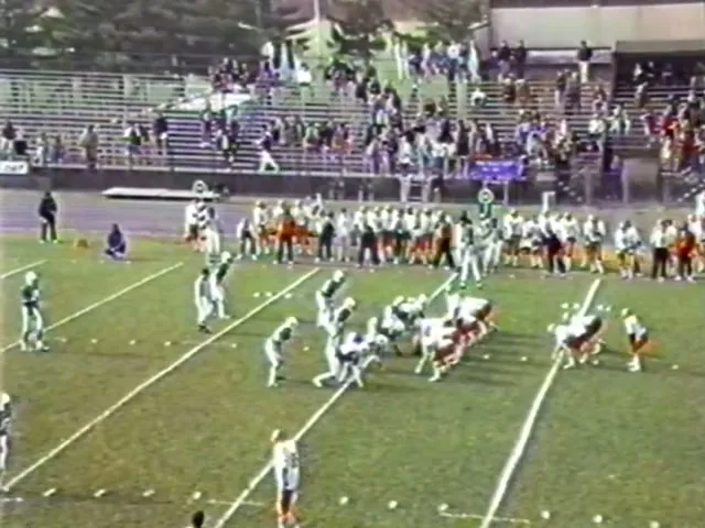 A videotape frame from 1987: the two teams lined up on the field, a crowd in the stands behind.