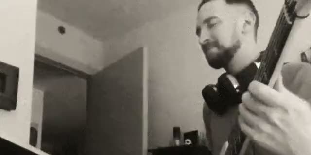 Alex playing bass at home, headphones around his neck, in black and white.